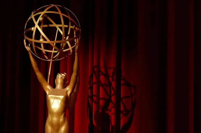 A silhouette and shadow of an Emmy award is shown in front of a red stage curtain.